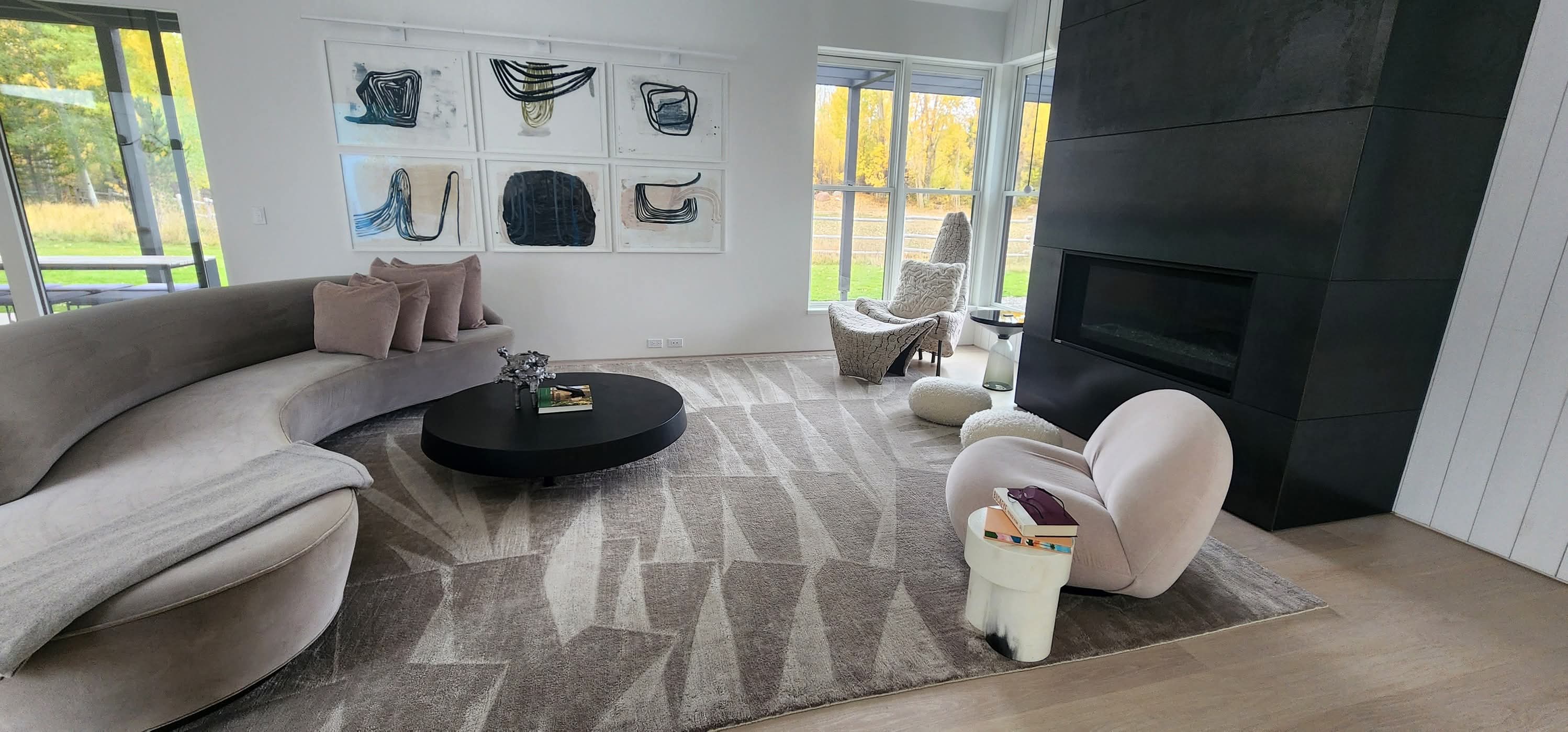 Modern living room with curved sofa, black fireplace, geometric rug, and abstract wall art.